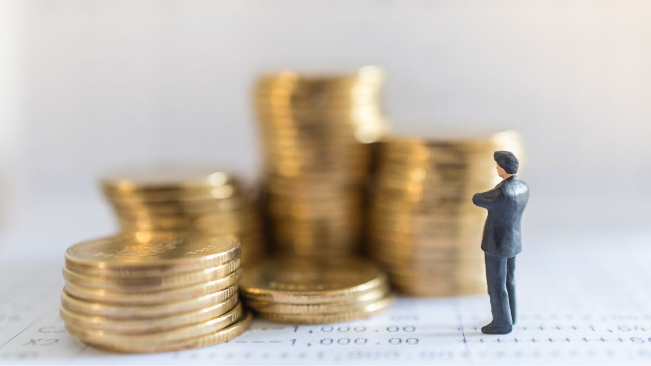 積まれた硬貨の前に立つミニチュアの男性の画像