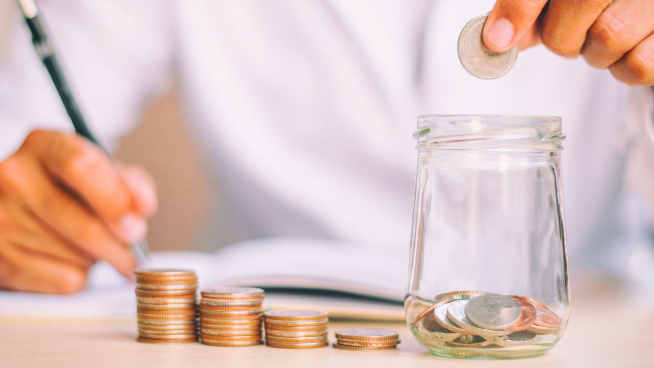 瓶に硬貨を入れ、書き物をしている手元の画像