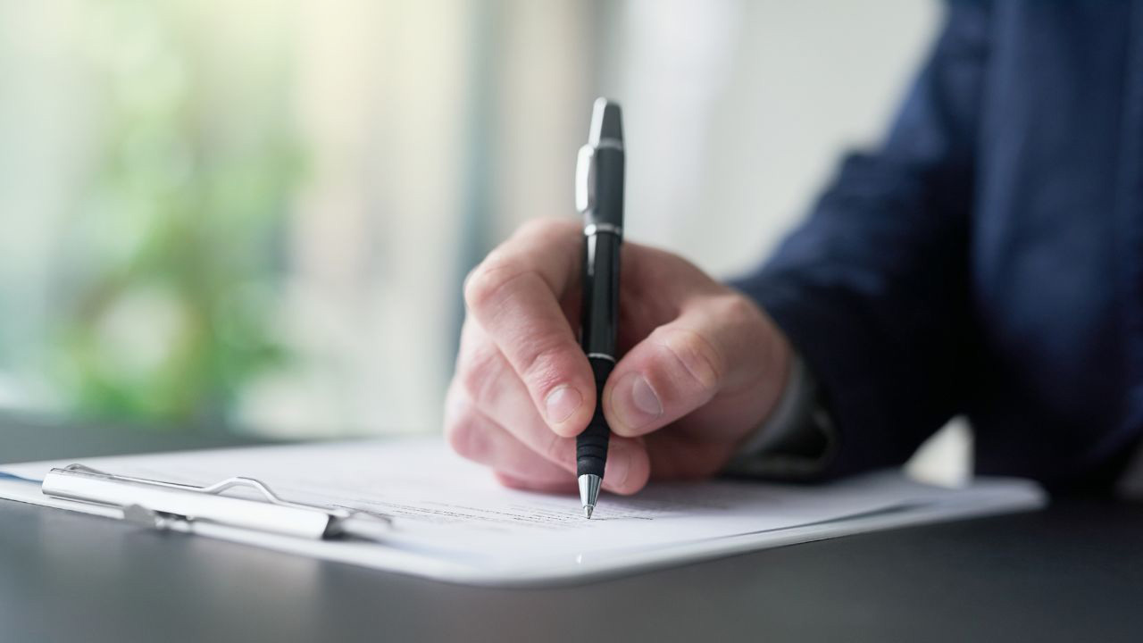 書類にペンで記入している手元の画像
