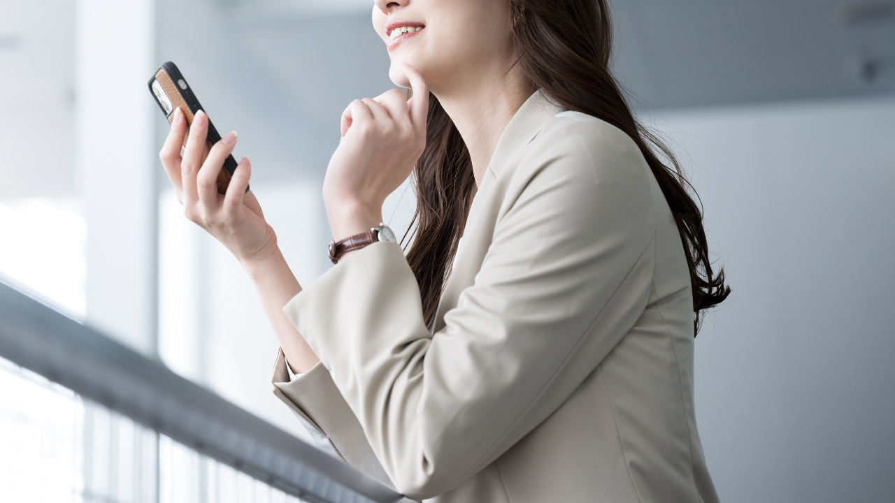 スーツを着た女性がスマホを眺める画像