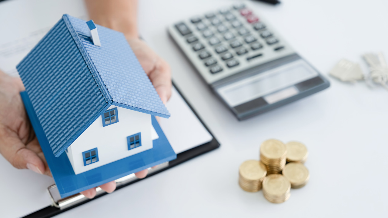家の模型と電卓、コインが並ぶ画像