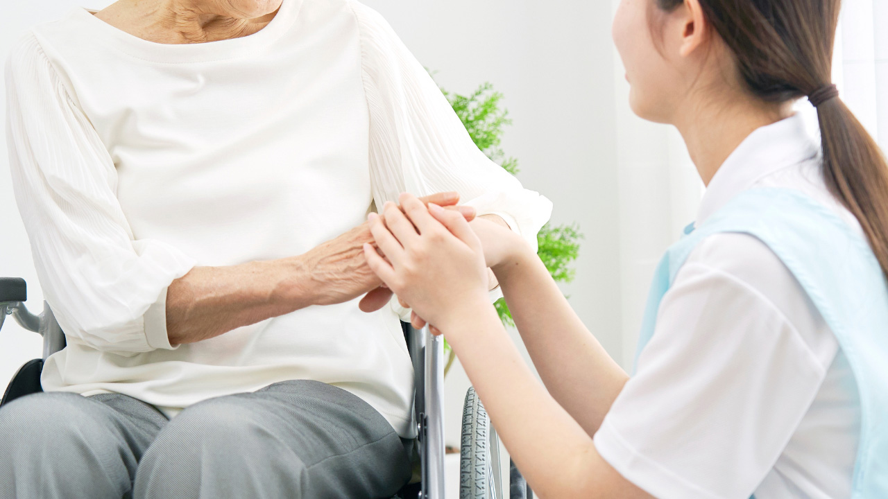 車椅子の高齢者と介護士が手を取り合っている画像