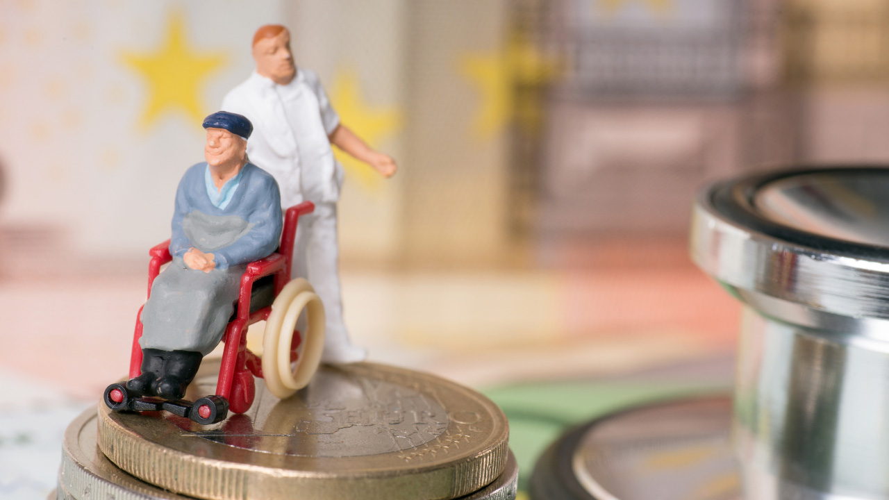 車椅子に座る人とその後ろに立つ介護者のミニチュアフィギュアが硬貨の上に置かれている画像