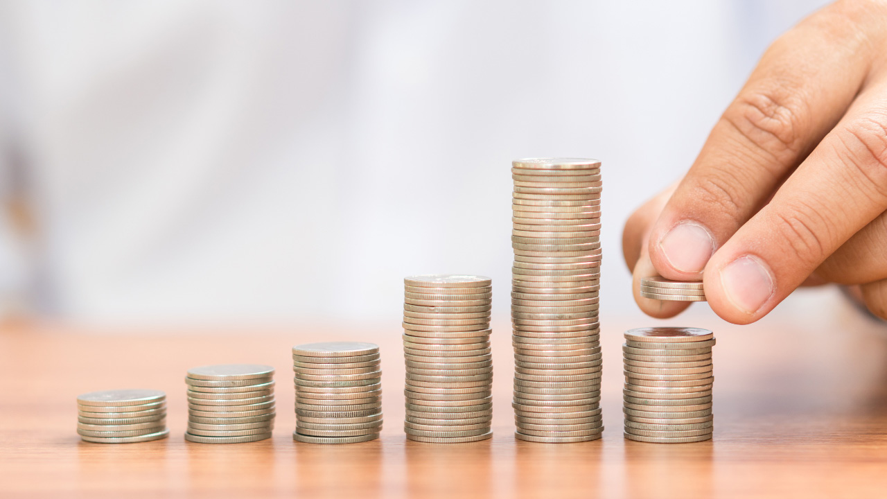 テーブルの上に積み重ねられた硬貨とそれを手で追加している様子の画像