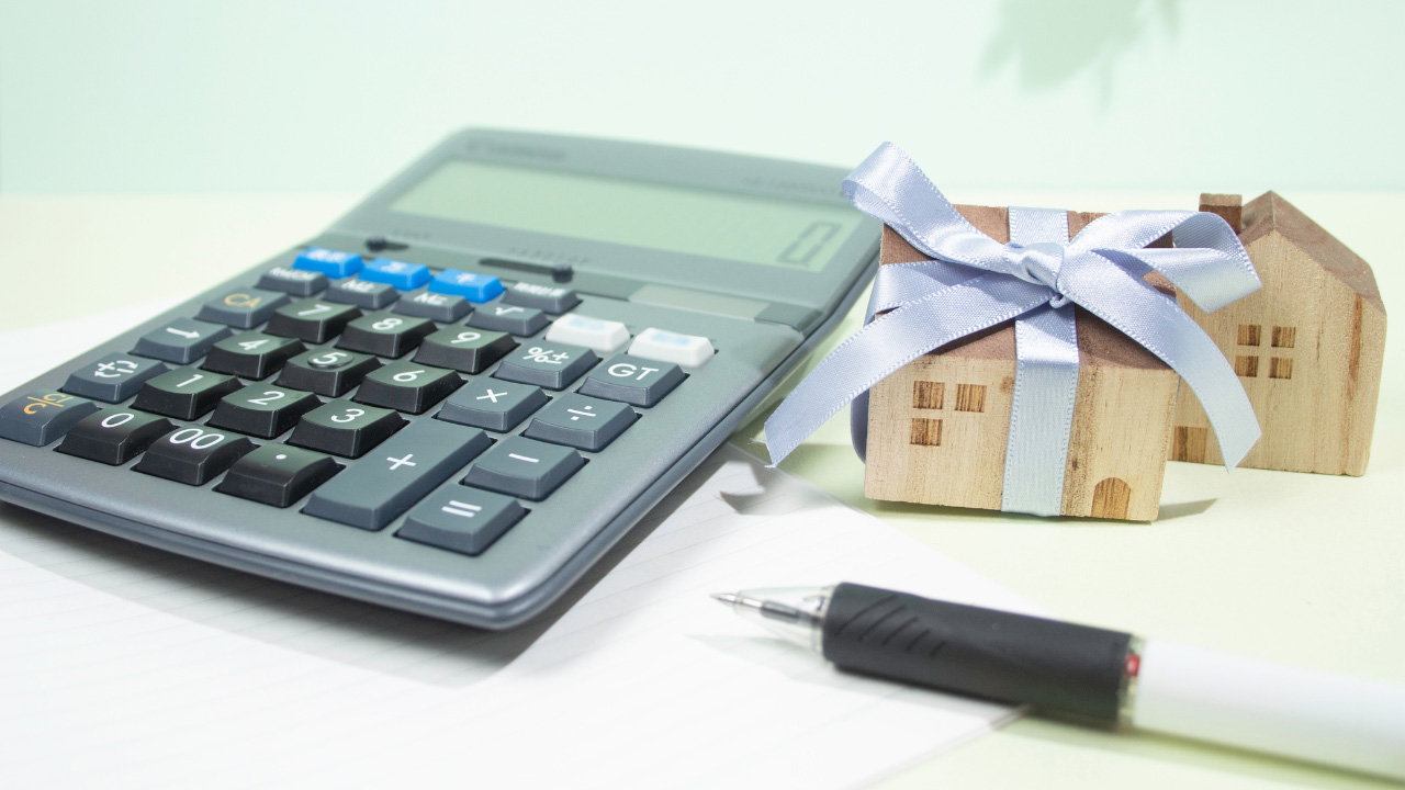 電卓、ペン、リボンがかけられた木製の家の模型が置かれた画像