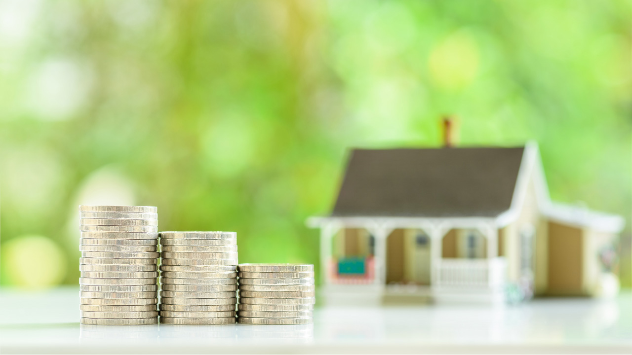 積み重ねられた硬貨と背景にミニチュアの家が写っている画像