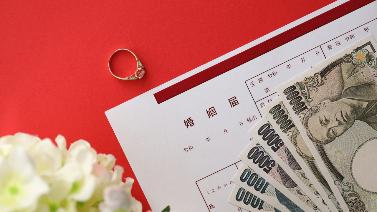 婚姻届、指輪、紙幣、花が並べられた画像