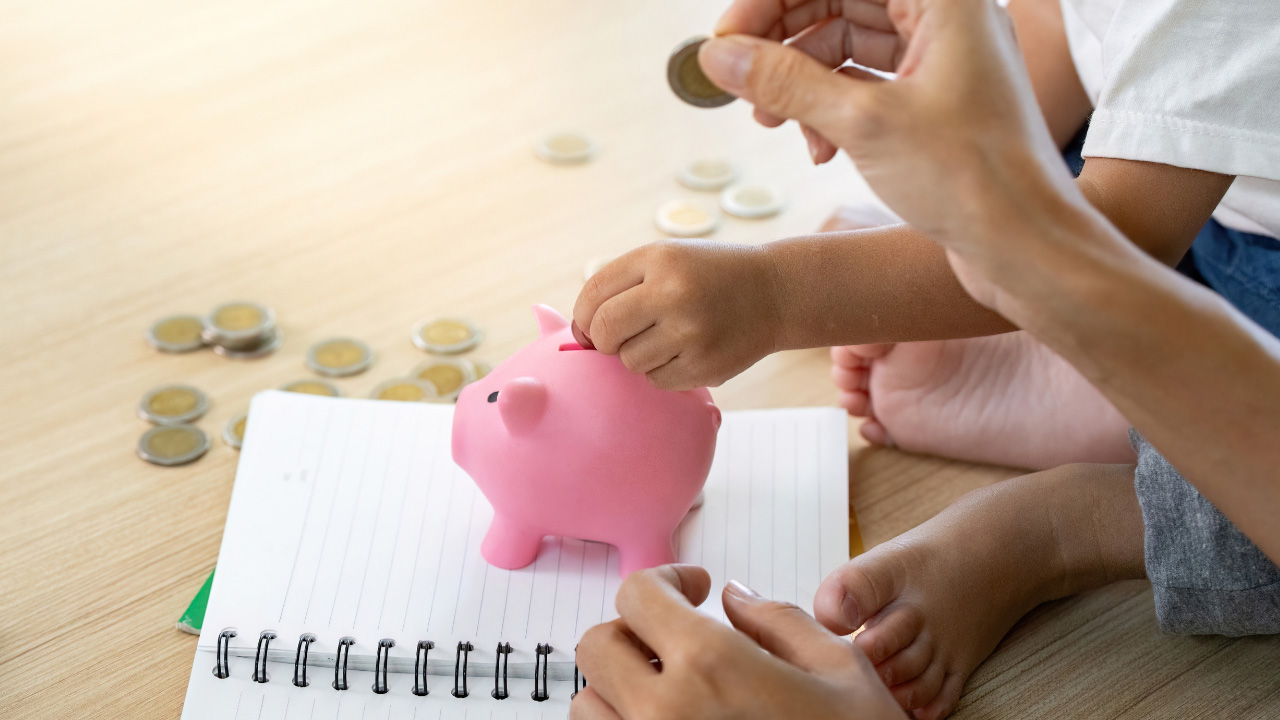 子どもと大人が貯金箱にお金を入れている画像